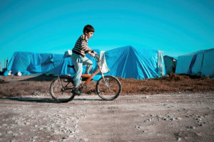A child rides a bike past tents of a refugee camp